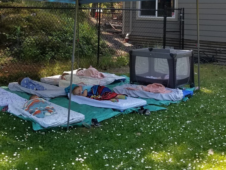 "Children peacefully napping outdoors under a canopy tent on mats in a sunny grassy backyard, surrounded by fresh air and nature — showing the real-life benefits of short daytime power naps for brain health and recovery"